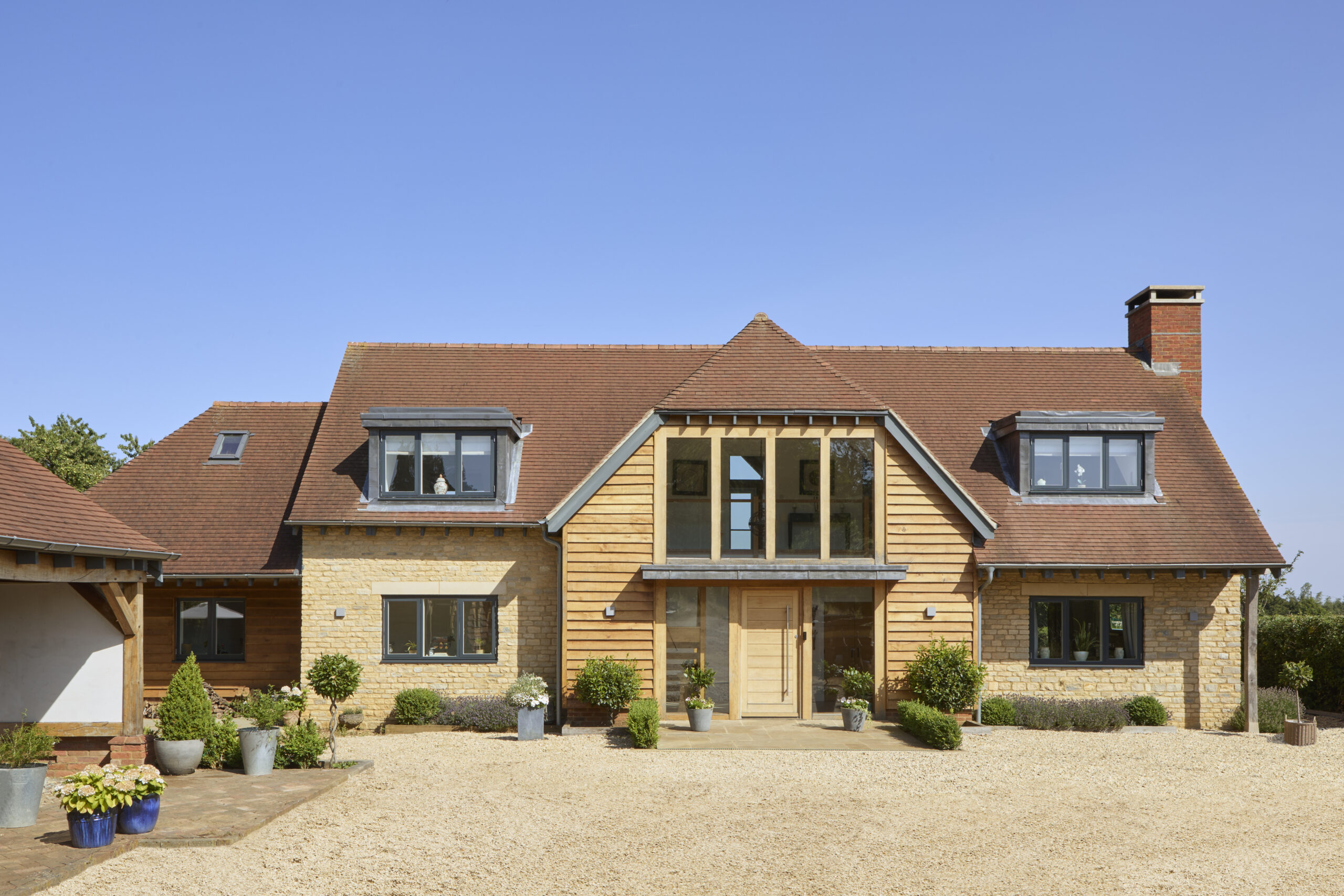 Exterior view new build home showing oak cladding, Cotswold stone and glazing.